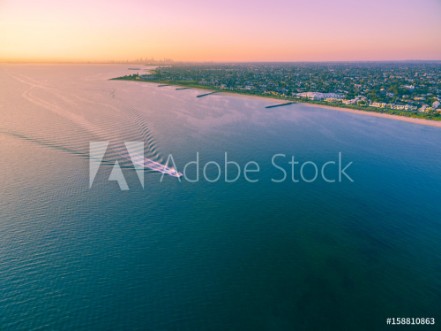 Picture of Aerial view of boat sailing across Port Phillip bay with Melbourne coastline and suburban areas in the background at beautiful sunset